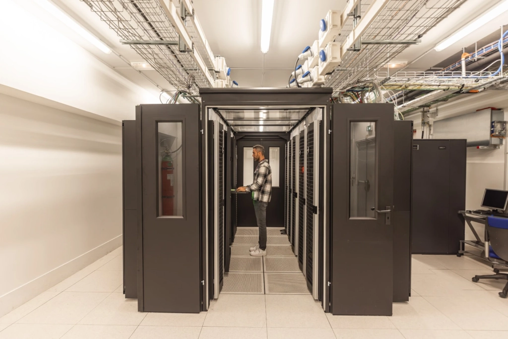 Technicien informatique intervenant dans une salle serveurs équipée de baies informatiques et de câblage réseau.